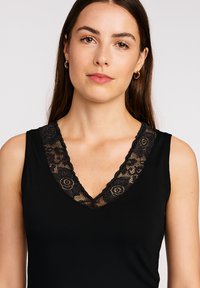 Black sleeveless top with a V-neck design featuring intricate black lace trim along the neckline. Smooth fabric, fitted shape.