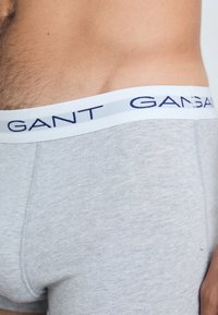 Shorts boxers en coton gris avec une ceinture blanche portant l'inscription "GANT" en lettres bleu marine, mettant en avant une texture douce et un design ajust�é.