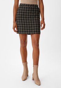 Schwarz-weißer karierten Minirock mit taillierter Passform, glatter Textur und einem Bund; kombiniert mit beigen Knöchelstiefeln mit einem quadratischen Absatz.