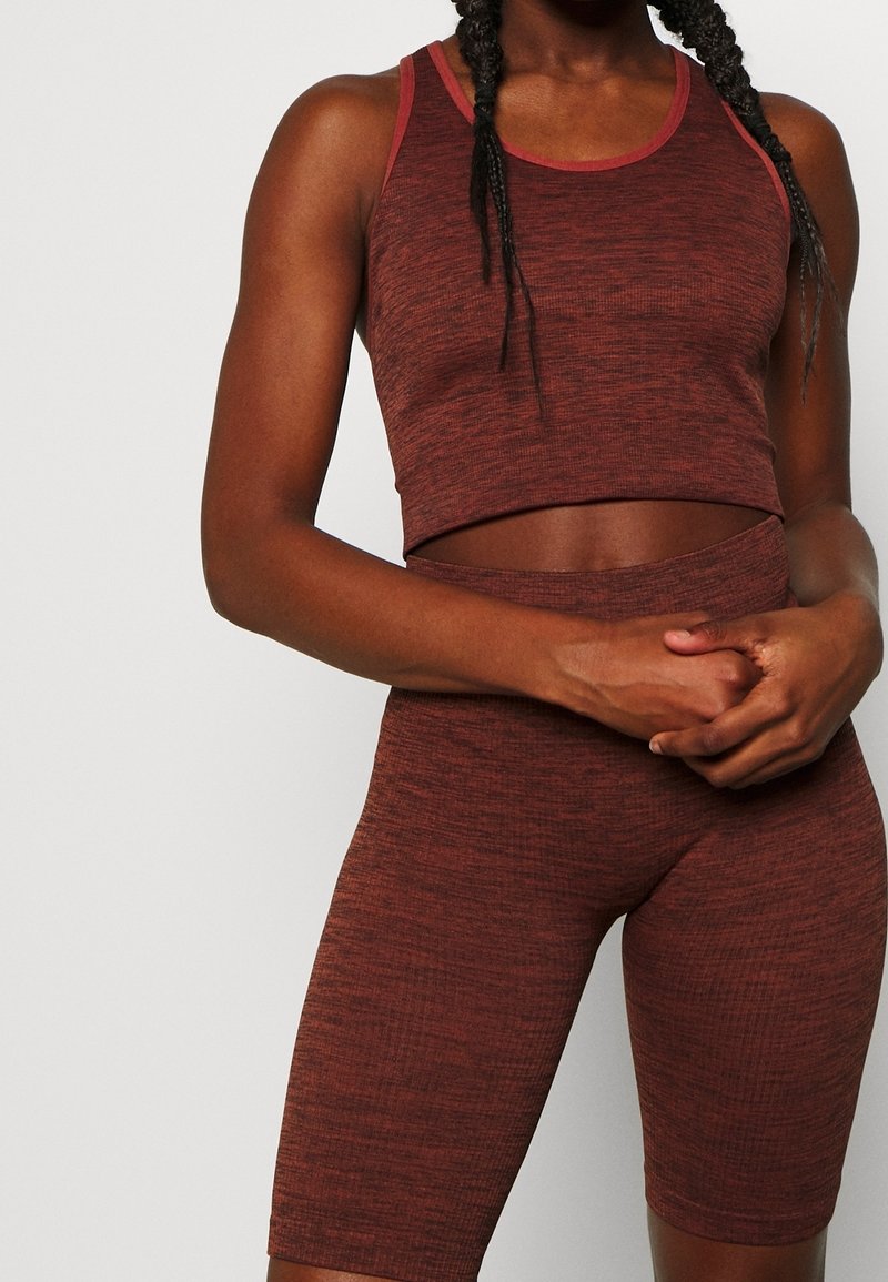 Brun struktureret crop top med kontrasterende rød halsudskæring, parret med matchende tætsiddende shorts, begge lavet af strækbart stof.