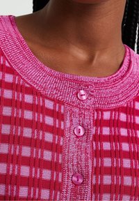 Röd och rosa stickad topp med ribbat mönster, rutigt mönster och tre rosa knappar fram. Bred, rund hals.