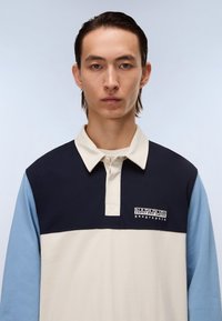 Polo tričko s dlouhým rukávem v námořnické modré, krémové a světle modré barvě. Má límec na knoflíky a vyšitý logo na hrudi. Texturovaná tkanina.