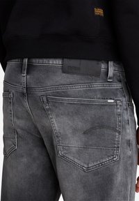 Grå denimjeans med slim fit, subtil blekning och bakfickor. Varumärket syns på midjebandet i en texturerad svart etikett.