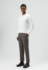 Witte blouse met lange mouwen, grijze geplooide broek en bruine loafers. Gladde stof met een ontspannen pasvorm, subtiel patroon op de broek.