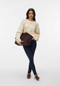 Maglione lavorato a maglia con base color crema e motivo geometrico colorato; borsa a tracolla in pelle marrone con texture liscia; jeans scuri e scarpe marroni.