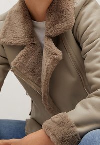 Beige nepbont kraagjacket met een gestructureerd leren lichaam, voorzien van een diagonale ritssluiting en pluchen voering op de kraag en manchetten.