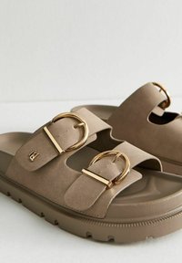 Beiga mocka sandaler med två breda remmar, stora gyllene ringspännen och strukturerade bruna sulor med ett vågmönster.