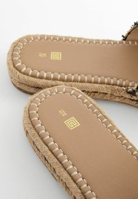 Gros plan sur des sandales espadrilles couleur beige clair avec des coutures beiges, des semelles en jute tressé, et des marquages de taille dorés "6.5/40" sur les semelles intérieures.