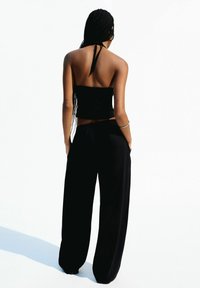 Top bandeau noir avec un lien autour du cou, associé à un pantalon noir à jambes larges. Tissu lisse avec une coupe décontractée, design minimaliste et sans motifs visibles.