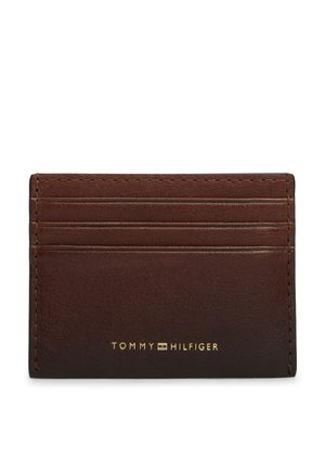 Brązowy skórzany portfel na karty z czterema miejscami na karty i złotym logo Tommy Hilfiger na środku z przodu.