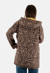 Veste en tissu peluche à imprimé léopard avec capuche, dotée d'une base beige et de taches brun foncé. Manches longues et coupe mi-longue.