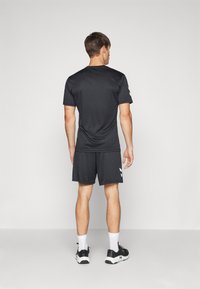 Camiseta deportiva negra de manga corta y pantalones cortos hechos de material ligero, con una textura suave. Acentos de logo blanco en los pantalones cortos.