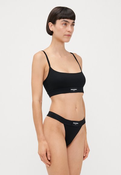 Black cropped bralette and thong set with thin straps. Features logo band on both pieces. Smooth, stretchy fabric and minimal design.