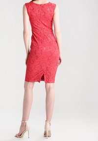 Robe en dentelle rouge avec un design sans manches, une silhouette ajustée et une fente dans le dos. Elle présente un motif en dentelle texturé et une doublure lisse en dessous.