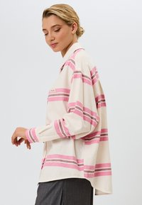 Let betjeningstrøje i letvægtsmateriale med en cremet base og pink og lilla vandrette striber, en foldet krave og en afslappet pasform.