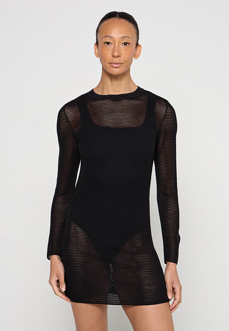 Vestido de punto negro con mangas largas, que presenta una trama suelta y abierta. Escote cuadrado y silueta ajustada. Textura semitranslúcida.