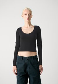 Sorte langermet crop topp med dyp utrigning og ribbestruktur. Kombinert med mørkegrønne bukser. Enkel, tettsittende design.