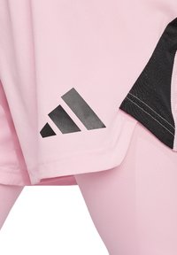 Gli shorts sportivi rosa presentano un pannello laterale nero con il distintivo logo a tre strisce grigio scuro di Adidas. Il tessuto è liscio ed elastico.