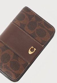 Καφέ δερμάτινο πορτοφόλι με υφασματοειδές σχέδιο, κλείσιμο σε σχήμα χρυσού πετάλου και μπεζ ραφές σε λευκό φόντο.