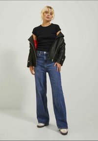 Μαύρο εφαρμοστό μπλουζάκι, υπερμεγέθη μαύρη δερμάτινη ζακέτα με κόκκινη επένδυση, ψηλόμεσα μπλε φαρδιά τζιν παντελόνια και ανοιχτόχρωμα Sneakers.