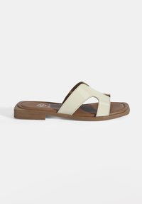 Plat slide sandaal met een lichtbeige gepatineerd bovenwerk, open neus met een lichte curve, en een bruine gevoerde binnenzool op een platte zool.