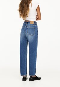 Högmidjade blå denimjeans med en rak passform. Har två bakfickor och en ljusblekning längs benen. Bakfickans detalj ingår.