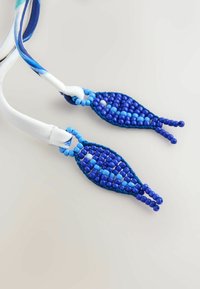 Colier albastru cu mărgele, cu forme ovale și nuanțe variate de mărgele albastre, cordon textil alb pentru agățare și accente decorative la capete.