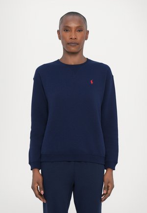Marineblå crewneck genser laget av mykt stoff, med ribbet halslinning og mansjetter, samt en liten rød logo på venstre bryst.