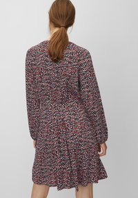 Šaty s dlouhým rukávem vyrobené z měkké tkaniny. Tmavé pozadí s barevným skvrnitým vzorem v červené, bílé a modré. Rozšířený lem.