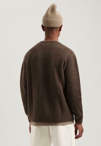 Bruin gebreid sweater met een losse pasvorm en ronde halslijn; gedragen met een lichtbeige beanie; zachte textuur, geribde manchetten en zoom.