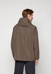 Brun vandtæt jakke med hætte, elastiske manchetter og en løs pasform. Glat stofstruktur med et ensfarvet design, set fra bagsiden.