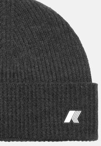 Berretto lavorato a maglia grigio con costine, con risvolto e una toppa con logo bianco sul lato. Il materiale sembra morbido e caldo.