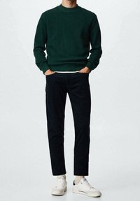 Pull vert côtelé associé à un pantalon bleu marine foncé et des baskets blanches. La tenue présente un col rond et une coupe décontractée.