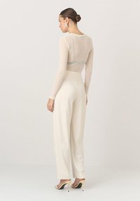 Przezroczysta bluzka z długim rękawem w jasnym beżu, zestawiona z białymi spodniami o wysokim stanie. Strój charakteryzuje się gładkim materiałem i dopasowanym krojem, uzupełniony czarnymi sandałami na obcasie.