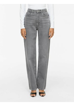 Person iført grå jeans med høj talje og lige ben med forlommer, en hvid langærmet top og sorte åbne hæle.