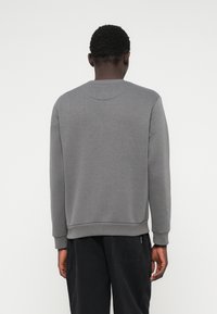 Sivý sweatshirt s okrúhlym výstrihom, dlhými rukávmi a rebrovanými manžetami. Vyrobený z mäkkej, štruktúrovanej tkaniny, s bežným strihom a minimálnym zdobením.