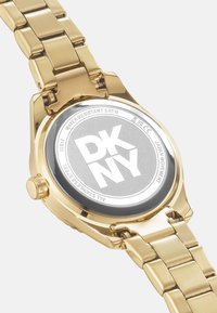 Orologio in acciaio inossidabile dorato con bracciale a maglie, caratterizzato da un fondello circolare argentato con il logo "DKNY" e una valutazione di resistenza all'acqua di 5 ATM.