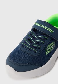 Mørkeblå sneakers med mesh-stof, grønne detaljer og en hvid sål. Har en rem og traditionelle snørebånd for en sikker pasform.