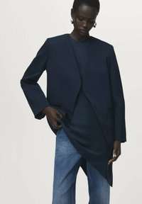 Laivastonsininen bleiseri, jolla on tyylikäs ja moderni leikkaus; villa materiaalia, avomalli ja sivutaskut. Yhdistetty tumman yläosan ja vaaleansinisten farkkujen kanssa.