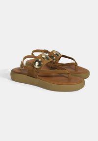 Braune Wildleder-Sandalen mit einer flachen, abgerundeten Sohle und drei großen metallischen runden Akzenten im Obermaterial. Verstellbarer Knöchelriemen inklusive.