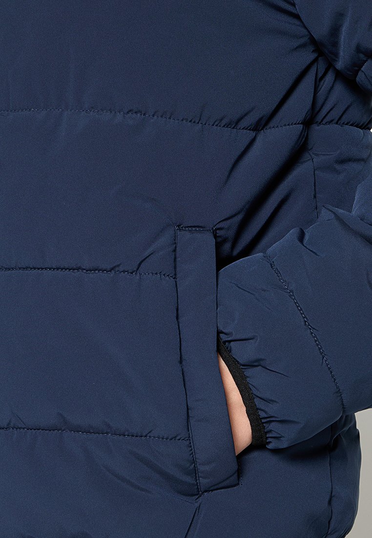 Veste matelassée navy avec un design en piqué, dotée d'une poche latérale et d'une texture de tissu douce. La veste a une coupe droite et un col montant.