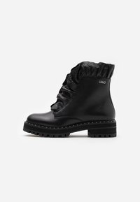 Botines negros de cuero con puño de tejido texturizado, que presentan un detalle de costura blanca y una suela robusta para mayor tracción.