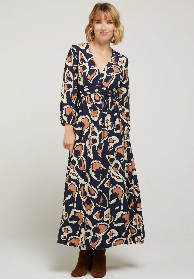 Robe maxi à manches longues, décolleté en V, de couleur bleu marine, avec un motif dans des tons de pêche et de crème. Présente une taille froncée et une silhouette fluide.