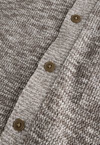 Gebreid bruin en beige stof met een gestructureerd patroon, met vier ronde bruine knopen langs de voorflap.