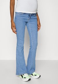 Calças de ganga azul-claro com corte à boca-de-sino, apresentando um design clássico de cinco bolsos, com desgaste leve e uma cintura de altura média, combinadas com ténis verdes e pretos.