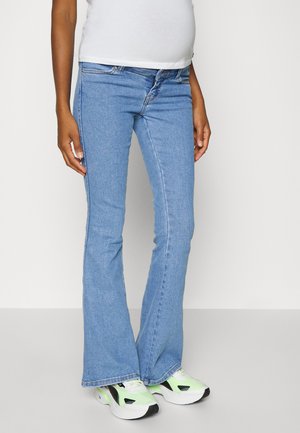 Calças de ganga azul-claro com corte à boca-de-sino, apresentando um design clássico de cinco bolsos, com desgaste leve e uma cintura de altura média, combinadas com ténis verdes e pretos.