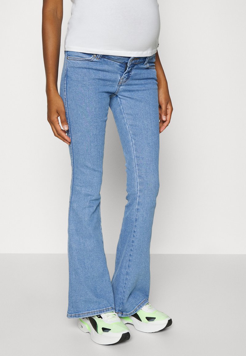 Calças de ganga azul-claro com corte à boca-de-sino, apresentando um design clássico de cinco bolsos, com desgaste leve e uma cintura de altura média, combinadas com ténis verdes e pretos.