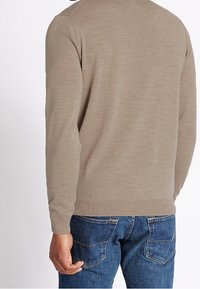 Béžový pletený svetr s dlouhými rukávy, kulatým výstřihem a žebrovaným spodním lemem. Nošený s modrými džínami z denimu, které mají zadní kapsy.