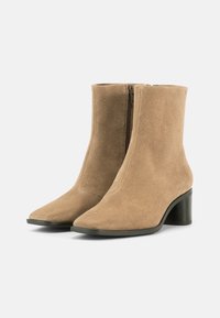 Beige suede ankle boots with a pointed toe, side zipper, and a block heel. Smooth texture and minimalist design.