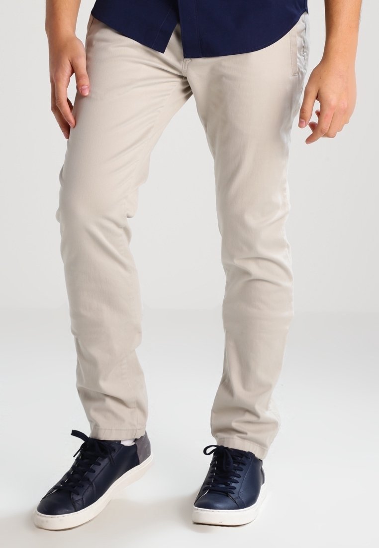 Světlé béžové kalhoty vyrobené z bavlněné směsi, slim fit design, v kombinaci s nízkými námořnickými teniskami s bílými podrážkami a tkaničkami.